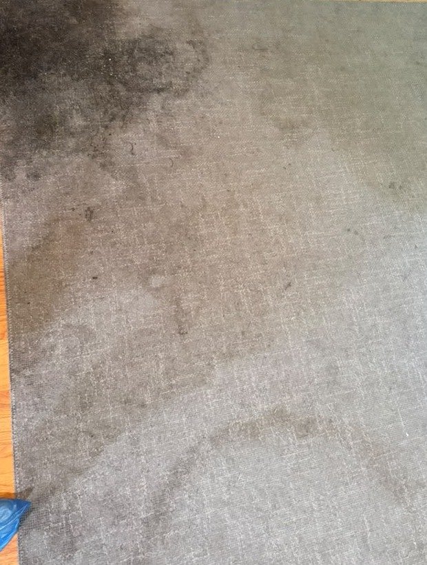Close-up of a gray rug corner heavily soiled with dark traffic stains before cleaning
